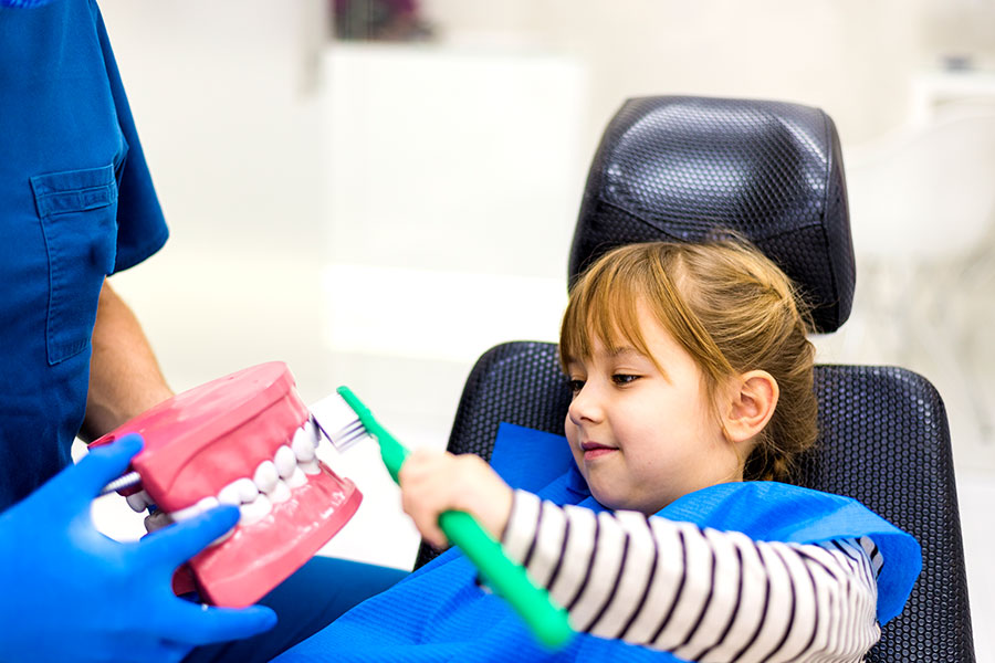 Young girl sitting in dentist chair holding toothbrush.