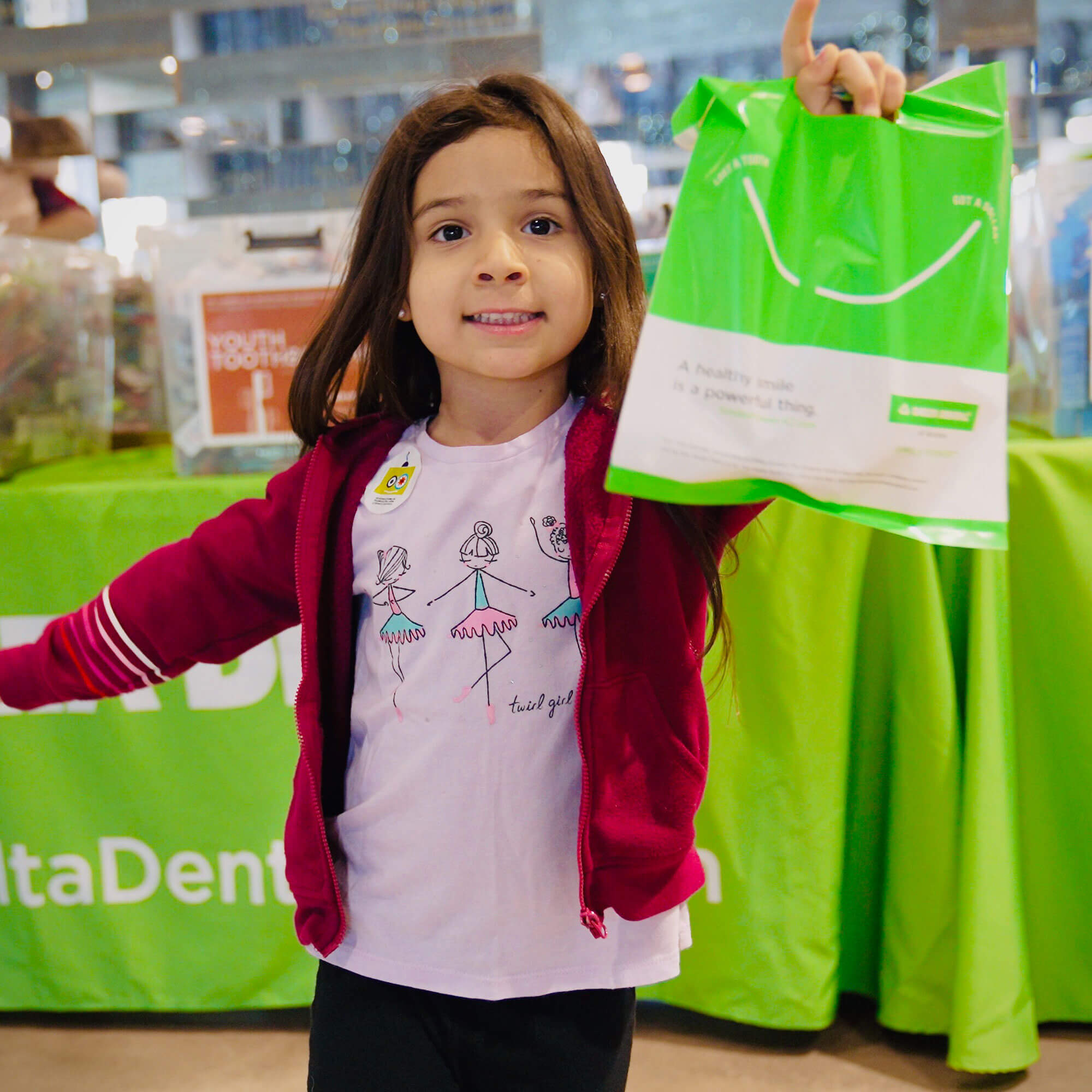 A young girl happily holds a bag of dental supplies, ready to take care of her teeth and maintain a healthy smile.