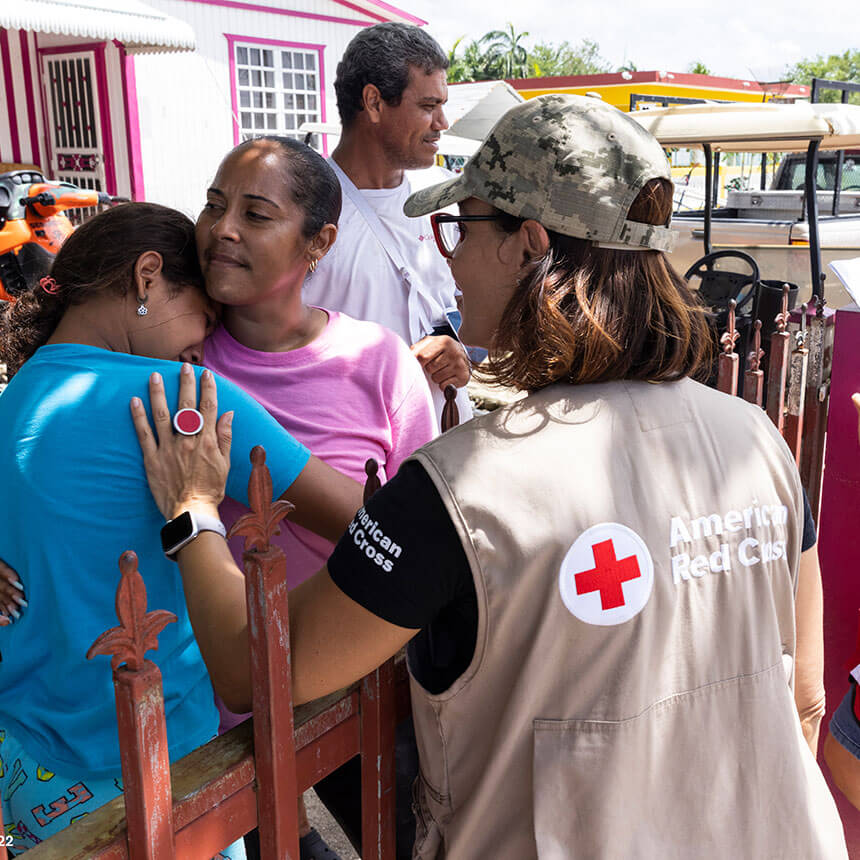American Red Cross volunteers in vests are providing assistance to community members, some of whom are embracing in relief or gratitude.