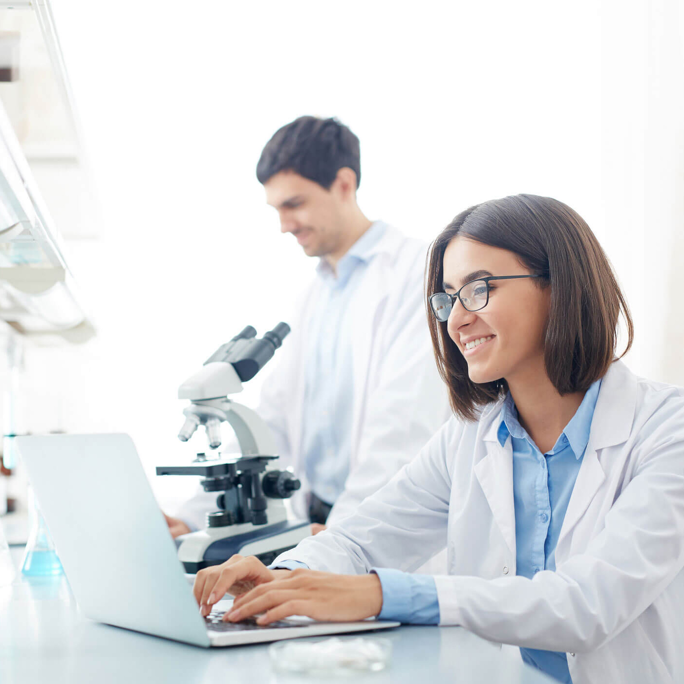 A woman and a man in lab coats collaborating on a laptop.