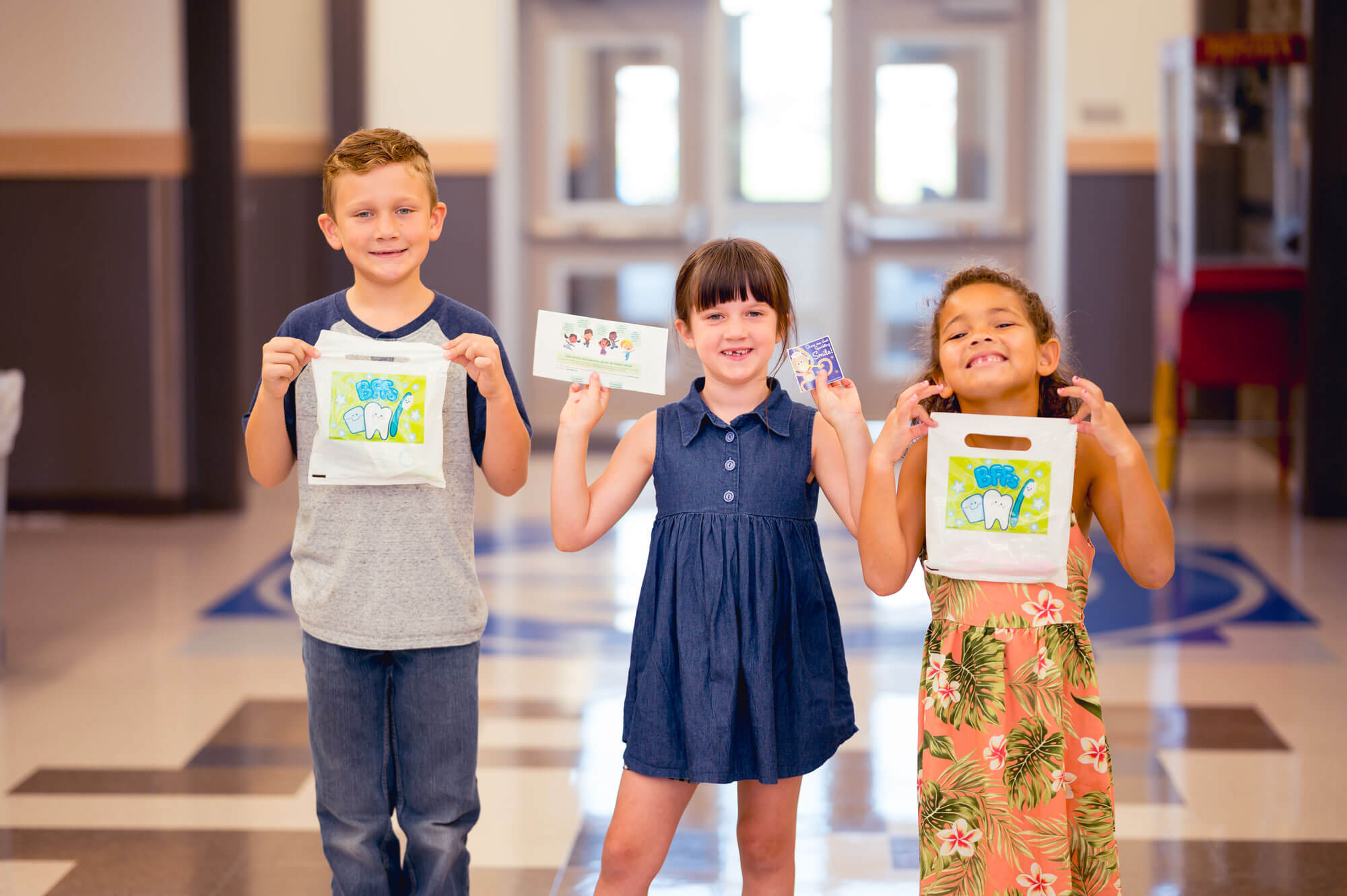 Three kids holding up cards in a hallway.